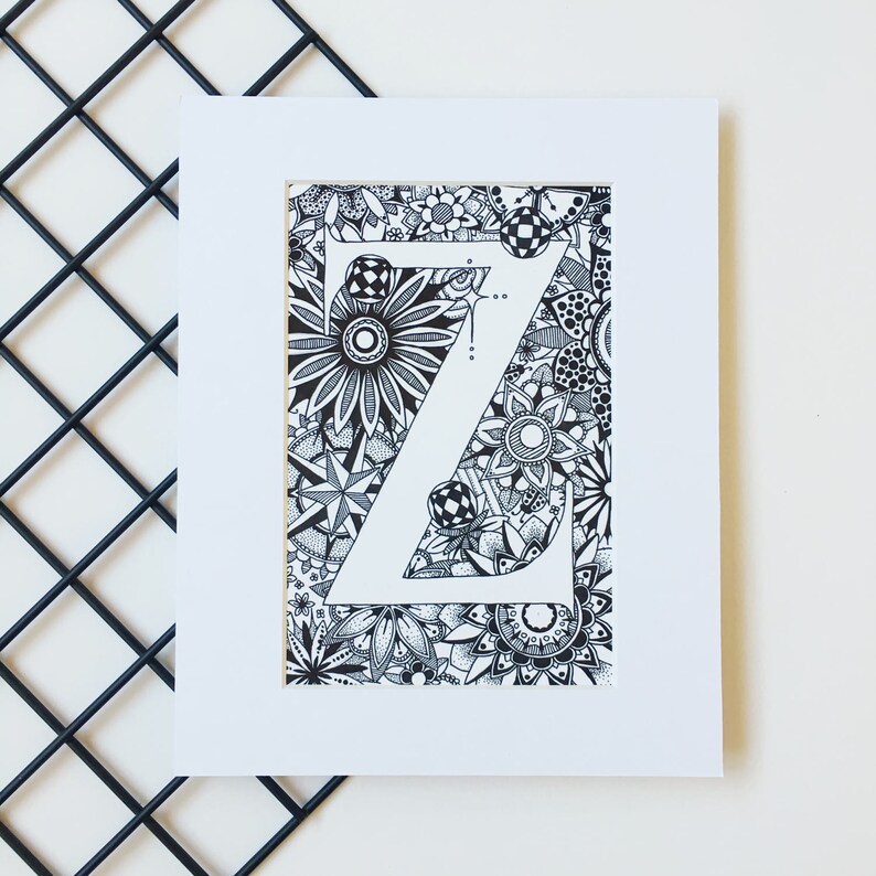 May include: A black and white illustration of the letter Z surrounded by intricate floral designs. The letter is outlined in white and the background is filled with black and white flowers, leaves, and swirls.