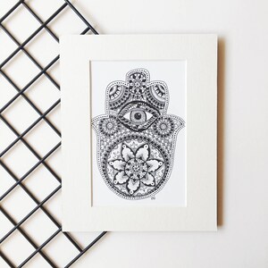 May include: A black and white hand-drawn illustration of a hamsa, also known as the Hand of Fatima, with a detailed mandala design and an eye in the center.
