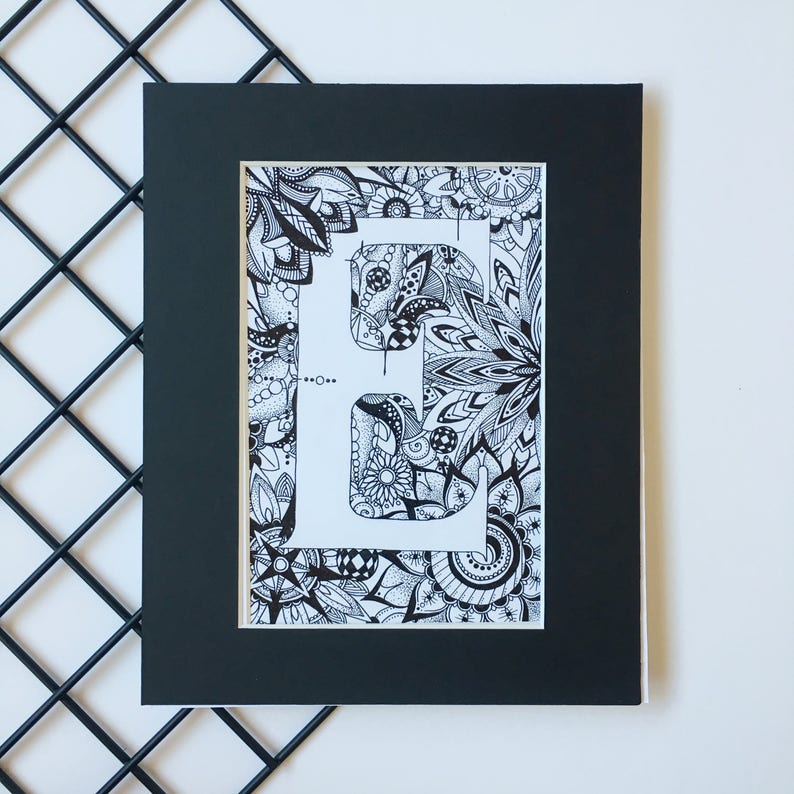 May include: Black and white framed print of the letter E surrounded by intricate floral designs.