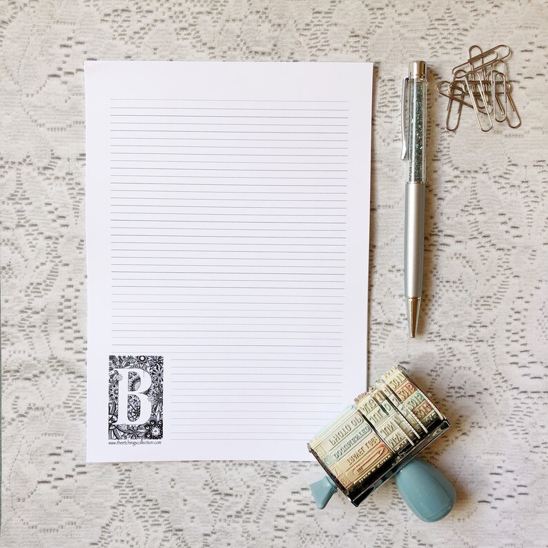 May include: A white sheet of lined paper with a black and white illustration of the letter "B" in the lower left corner. A silver pen with glitter inside is on the right side of the paper. A blue and silver stamp with various numbers and letters is in the lower right corner.