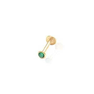 May include: A gold body piercing with a small green gemstone.