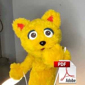May include: A bright yellow plush puppet with soft fur, large white eyes with dark pupils, dark eyelids, and a small black nose. The puppet has pointed ears with red inner accents and a small open mouth, appearing as a character with a fuzzy texture.