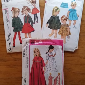 May include: Three vintage sewing patterns for children's clothing. Two Simplicity patterns feature illustrations of girls in dresses and skirts. The third is a McCall's pattern for a Barbie doll costume. The patterns are on a wooden surface.