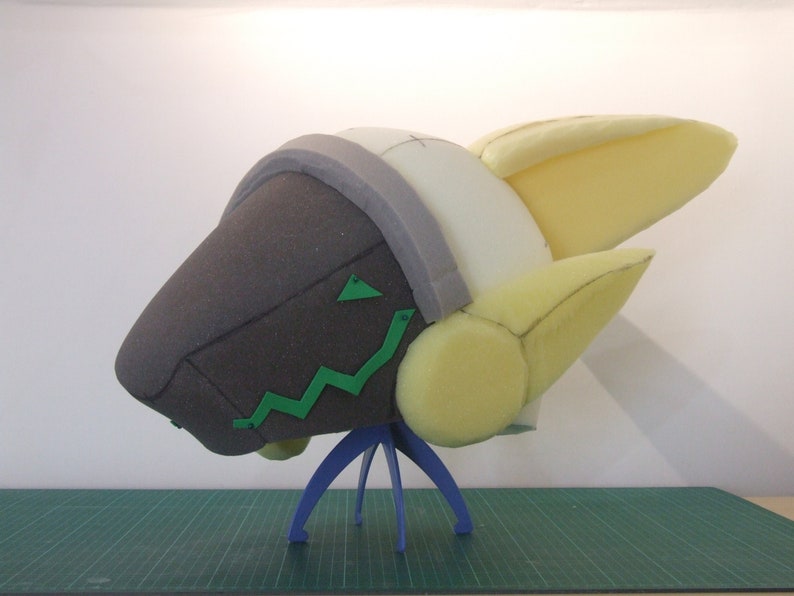 May include: A foam head sculpture with a yellow and white head and a brown face. The head is on a blue stand.