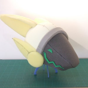 May include: A foam head sculpture with a gray and white helmet and green details. The sculpture is on a green cutting mat.