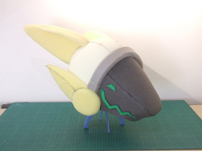 May include: A foam head sculpture with a gray and white helmet and green details. The sculpture is on a green cutting mat.