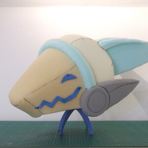 May include: A foam sculpture of a cartoon character's head with a blue and white helmet, gray ears, and blue details on the face. The sculpture is mounted on a blue stand.