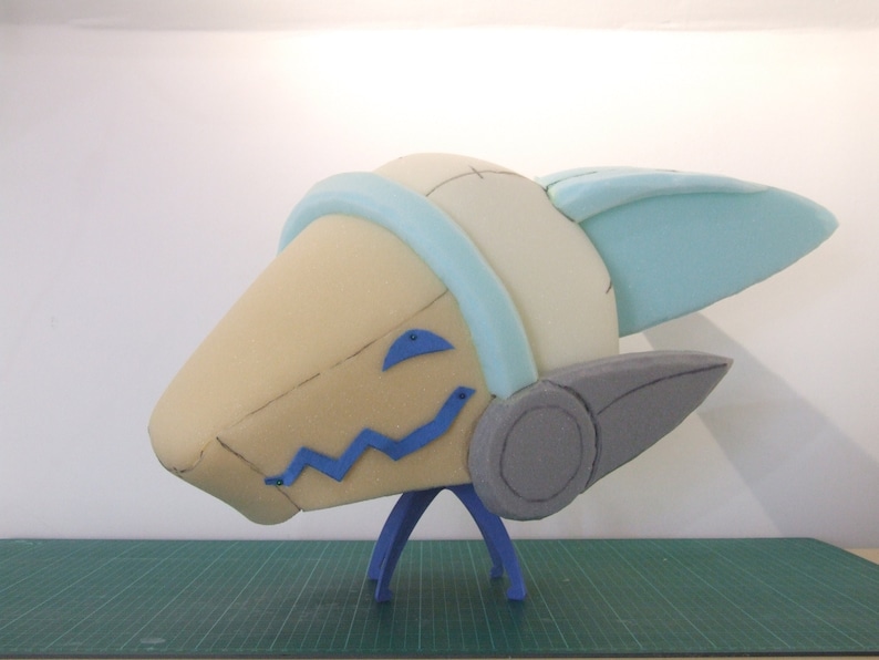 May include: A foam sculpture of a cartoon character's head with a blue and white helmet, gray ears, and blue details on the face. The sculpture is mounted on a blue stand.