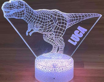 May include: A 3D-style LED night light featuring a Tyrannosaurus Rex dinosaur design. The light has a clear acrylic panel with a wireframe dinosaur and the name "LUCA" in purple. The base is a round, textured, glowing light.