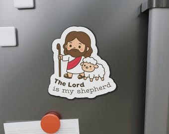 May include: A white sticker featuring a cartoon illustration of a shepherd with a staff and a sheep. The shepherd has brown hair and a beard, wearing a white robe with a red sash. The text "The Lord is my shepherd" is below the illustration.