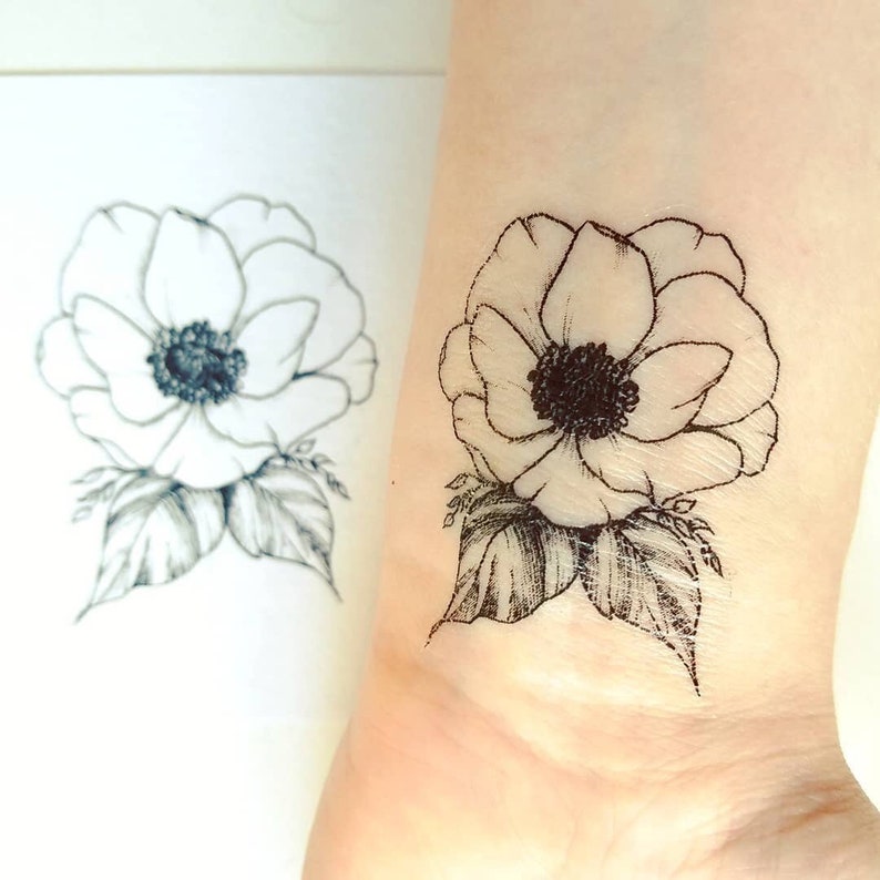 Puede incluir: Un tatuaje temporal en blanco y negro de una sola flor de an&eacute;mona con hojas.
