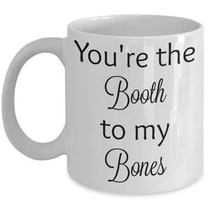 May include: White ceramic coffee mug with black text that reads "You're the Booth to my Bones".