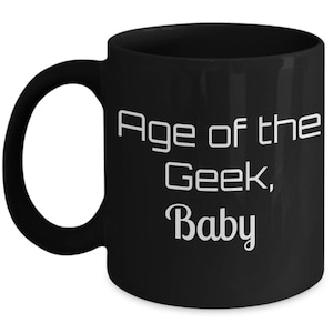 May include: Black coffee mug with white text that reads "Age of the Geek, Baby".