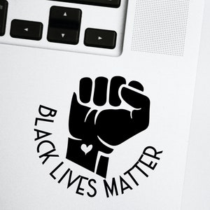 May include: Black Lives Matter sticker featuring a raised fist with a small heart on the wrist. The sticker is on a white laptop.