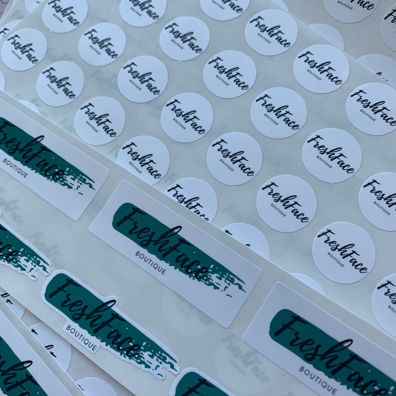 May include: A sheet of white round stickers with the text "FreshFace Boutique" printed in black. There are also larger rectangular stickers with the same text in black, but with a green brushstroke behind it.
