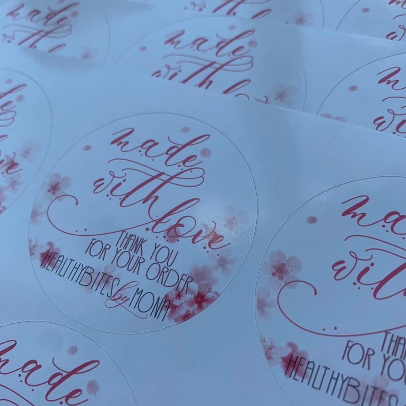May include: Round sticker with pink watercolor floral design. The sticker says "made with love" in cursive script. Below the text is "Thank you for your order" and "HEALTHYBITES by MONA".