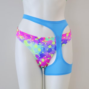 May include: A two-piece swimsuit set on a mannequin. The top is a crop top with a colorful pattern of pink, yellow, and blue spots. The bottoms are high-cut with a blue trim and a matching colorful pattern.