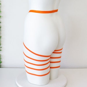 Op de afbeelding: Een wit mannequin met oranje banden om de benen en taille gewikkeld.