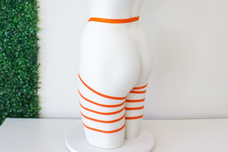 Op de afbeelding: Een wit mannequin met oranje banden om de benen en taille gewikkeld.