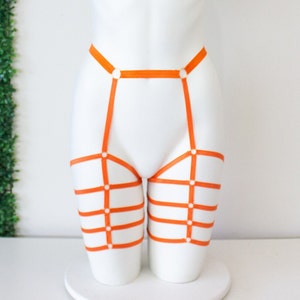 Op de afbeelding: Oranje lingerie harnas met banden en ringen. Het harnas is op een wit mannequins.
