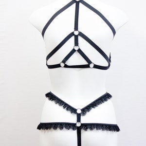 May include: Black lingerie set displayed on a white mannequin. The set features a harness top with ring details and a matching bottom with lace edging. The design is minimalist and elegant, with a focus on the interplay of lines and shapes.