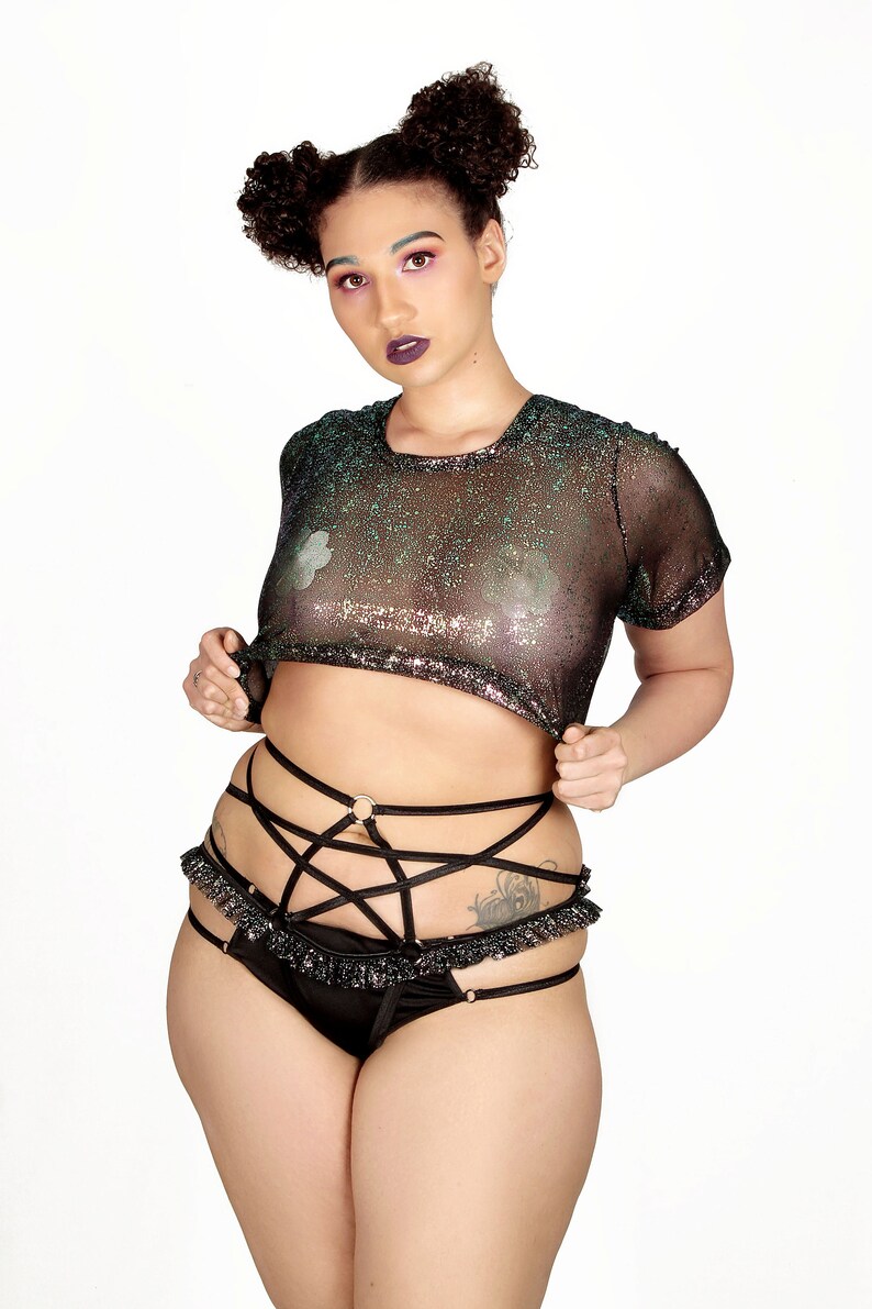May include: A black lingerie set featuring a sheer, short-sleeved top with iridescent glitter and a matching bottom with a strappy design and ruffled trim. The set includes gold-colored rings.
