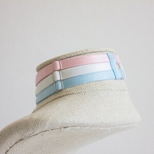 May include: A white fabric mannequin head with a light blue, white, and pink ribbon choker.