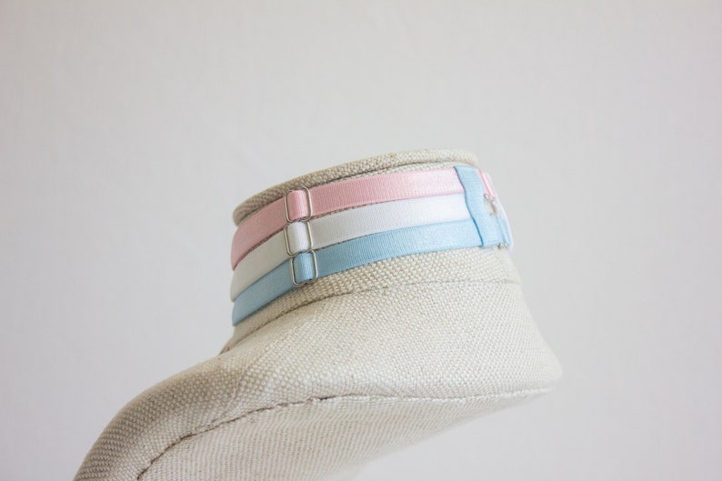 May include: A white fabric mannequin head with a light blue, white, and pink ribbon choker.