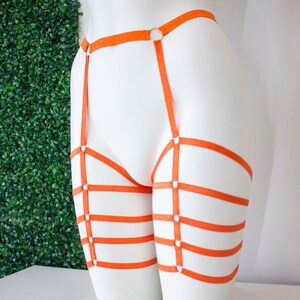 Op de afbeelding: Oranje lingerie harnas met meerdere banden en ringen. Het harnas is op een wit mannequins.