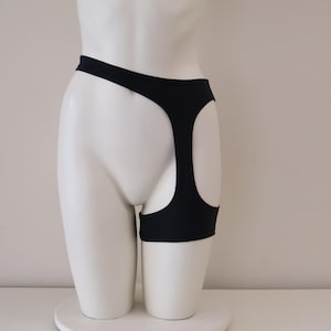 May include: Black underwear with a unique design, featuring cut-out details on the sides. The garment is displayed on a white mannequin, showcasing its shape and form. The background is a plain white.