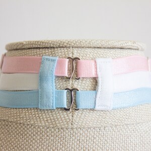 May include: A set of three adjustable bra straps in pink, white, and light blue. The straps have silver metal clasps.