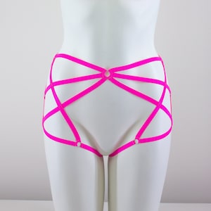 May include: Bright pink lingerie with a strappy design. The garment features multiple straps that intersect and connect with small circular rings. The lingerie is displayed on a white mannequin.