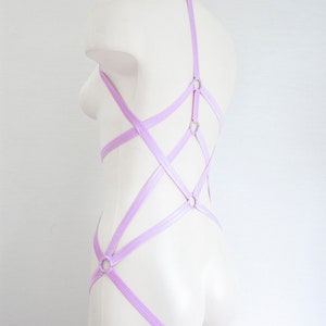 May include: A lavender colored body harness with multiple straps and silver metal rings. The harness is on a white mannequin.