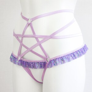 May include: A lavender lingerie harness featuring a five-pointed star design. The harness has a ruffled trim with iridescent glitter. The straps are thin and delicate, creating a unique and eye-catching look.