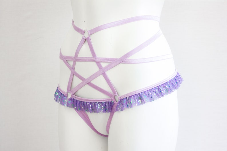 May include: A lavender lingerie harness featuring a five-pointed star design. The harness has a ruffled trim with iridescent glitter. The straps are thin and delicate, creating a unique and eye-catching look.