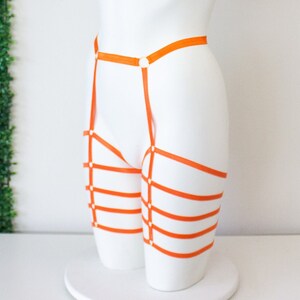 Op de afbeelding: Oranje lingerie harnas met meerdere banden en gespen. Het harnas is gemaakt van een zacht, rekbaar materiaal en is ontworpen om over de heupen en dijen te worden gedragen.