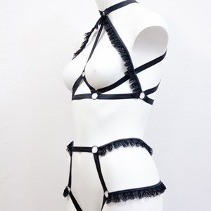 May include: Black lingerie set on a white mannequin. The set includes a halter top with lace trim and a matching high-waisted bottom. The lingerie features a strappy design with metal ring accents.