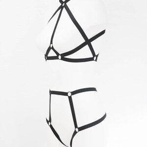 May include: Black lingerie set with straps and metal rings. The set includes a bra and a panty.