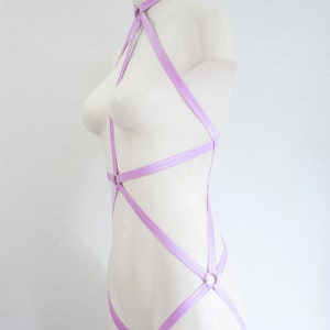 May include: A lilac-colored body harness with multiple straps and rings. The harness is made of a soft, stretchy material and is designed to be worn over the body.