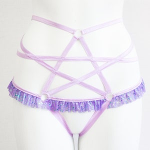 May include: A light purple lingerie set featuring a pentagram design. The set includes a waist harness with a star-shaped design and a matching thong. The waist harness has a ruffled trim with glitter accents.