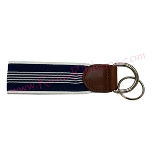 May include: A navy blue and white striped key chain with a brown leather loop and double silver key rings.