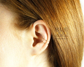 May include: A gold ear cuff with two thin hoops. The cuff is worn on the upper part of the ear, just above the cartilage.
