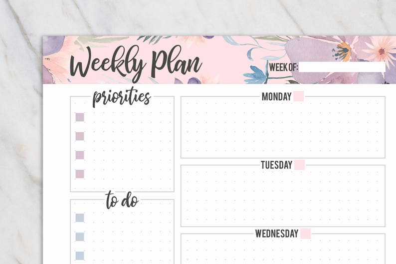 May include: A weekly planner with a floral design in pink, purple, and blue. The top of the planner reads "Weekly Plan" in black script. It includes sections for priorities and to-do lists, with spaces for each day of the week.