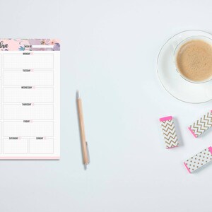 May include: A weekly planner notepad with floral accents, a pen, three erasers, and a cup of coffee on a white surface. The planner has sections for each day of the week, priorities, to-do lists, and notes.
