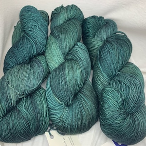 May include: Three skeins of teal blue yarn with a subtle green shimmer. The yarn is wound into balls and is ready to be used for knitting or crocheting.