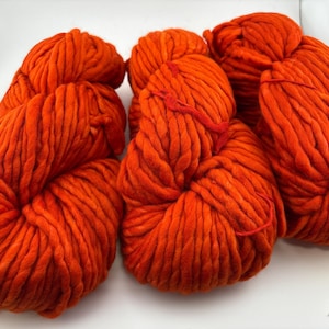 K&ouml;nnte beinhalten: Drei Str&auml;nge aus dickem, leuchtend orangefarbenem Garn, die nebeneinander angeordnet sind. Jeder Strang weist eine grobe, gedrehte Textur mit weichem Aussehen auf. Das Garn hat durchgehend eine einheitliche, helle orange Farbe.