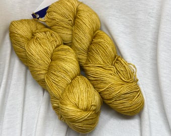 Könnte beinhalten: Zwei Knäuel goldgelbes Garn, eine weiche und luxuriöse Faser zum Stricken oder Häkeln.