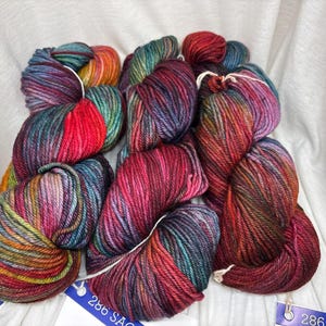 Puede incluir: Tres madejas de hilo te&ntilde;ido a mano con una paleta de colores variados en rojo intenso, magenta, verde azulado y amarillo dorado. Cada madeja est&aacute; retorcida y asegurada con un cordel blanco, acompa&ntilde;ada de una etiqueta azul y blanca 286 SAO.