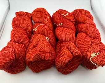 May include: Four skeins of vibrant orange yarn arranged in a row. Each skein features a twisted, multi-ply construction with a consistent, saturated color throughout. The yarn has a slight sheen and a textured appearance, with small white ties.