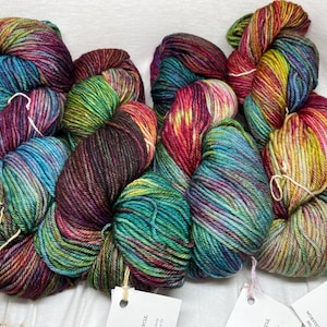 May include: Four skeins of colorful yarn in shades of teal, purple, red, and yellow. The yarn is arranged in a loose pile, with the ends of the skeins visible.